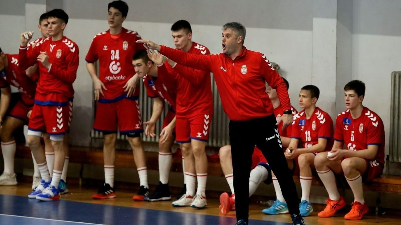 Serbia under-18 handball players celebrate together beside the bench