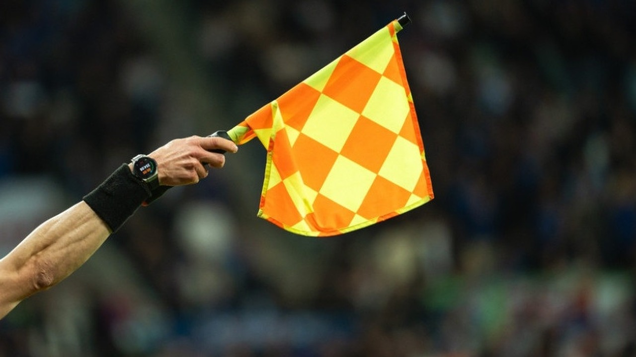 An assistant referee holds a yellow and orange flag